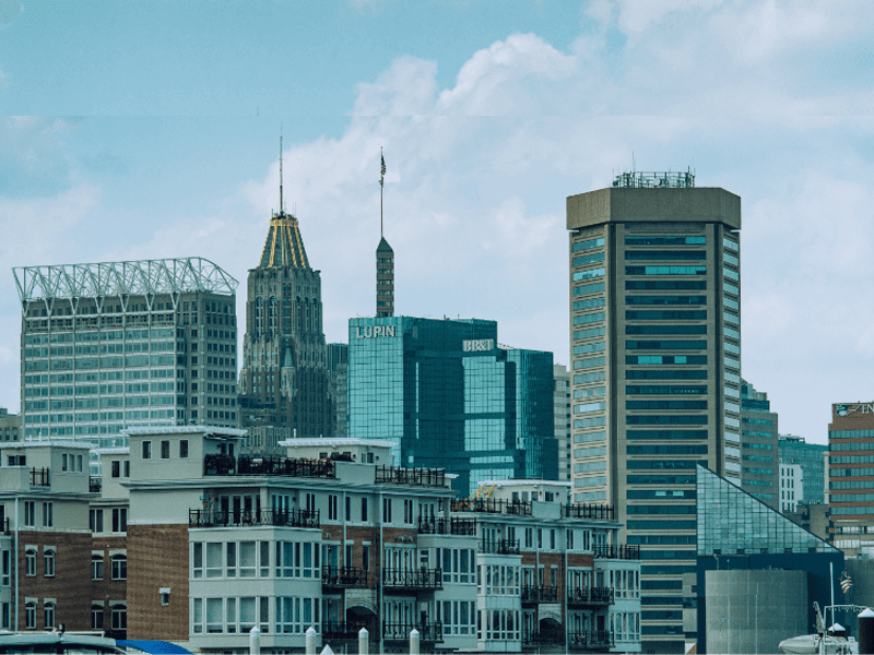 A city skyline with several tall modern and historic buildings under a cloudy blue sky, including apartments in the foreground and glass skyscrapers in the background.