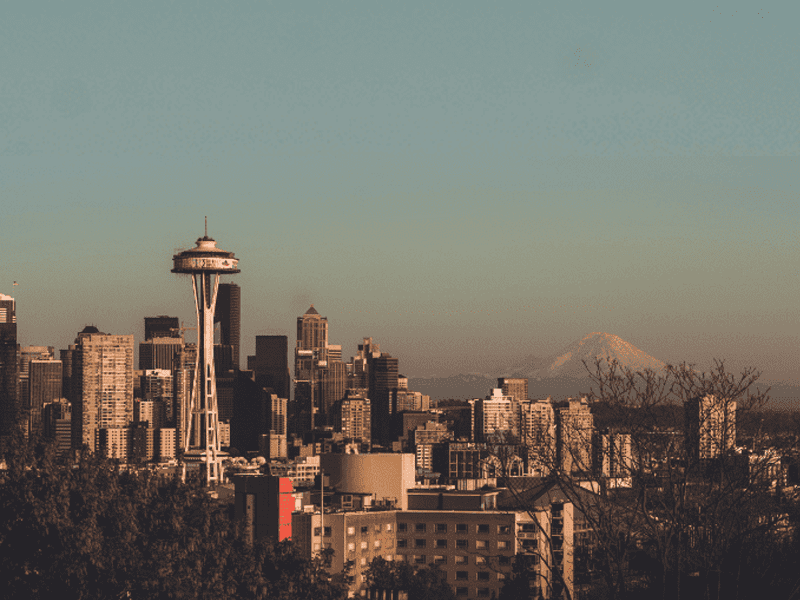 Seattle city skyline at sunset with the Space Needle prominent in the foreground and Mount Rainier visible in the background under a clear sky.