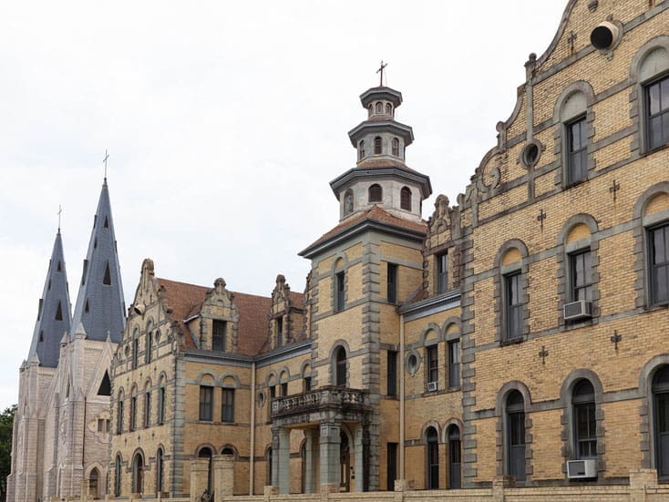 A historic brick and stone church complex featuring pointed spires, arched windows, and decorative architectural details, set against a cloudy sky.